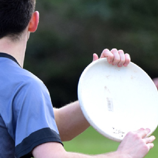 Photo from behind a person wearing a purple and black shirt holding a white frisbee